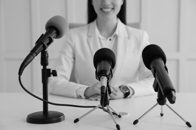 Image of Journalist conference. Businesswoman giving interview at table with microphones indoors, closeup. Black and white effect