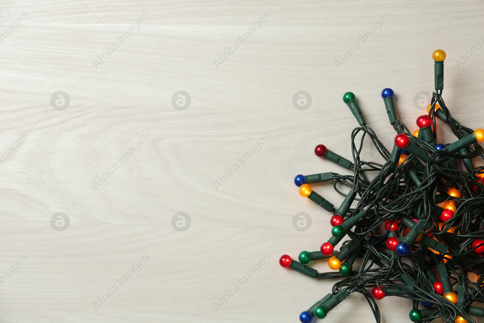 Photo of Beautiful glowing Christmas lights on white wooden background, top view. Space for text