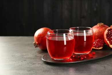 Photo of Tasty pomegranate juice in glasses and fresh fruits on grey table. Space for text