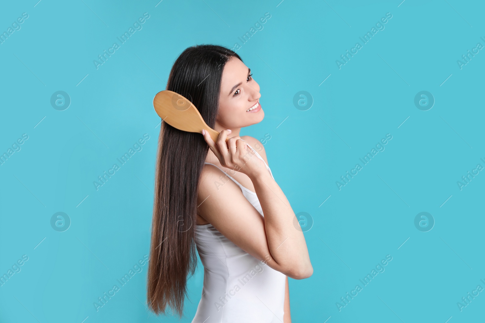 Photo of Beautiful smiling young woman with hair brush on color background