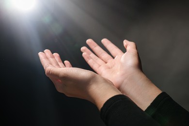Photo of Woman stretching hands towards light in darkness, closeup