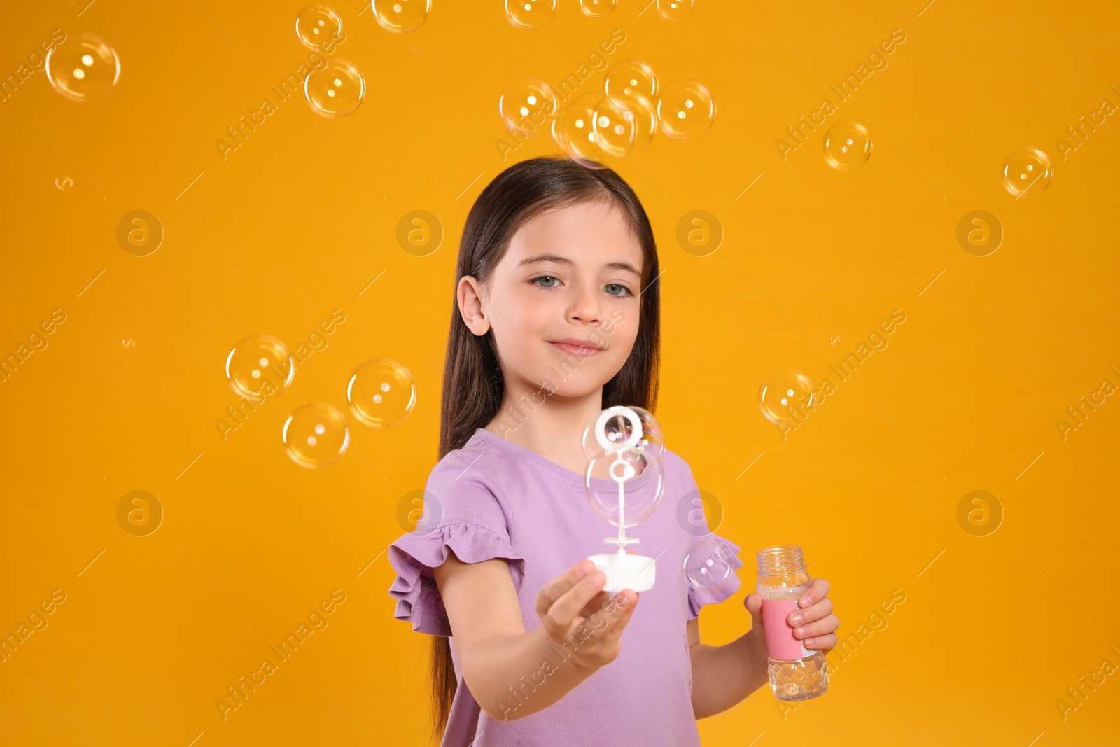 Photo of Little girl having fun with soap bubbles on yellow background