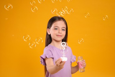 Photo of Little girl having fun with soap bubbles on yellow background