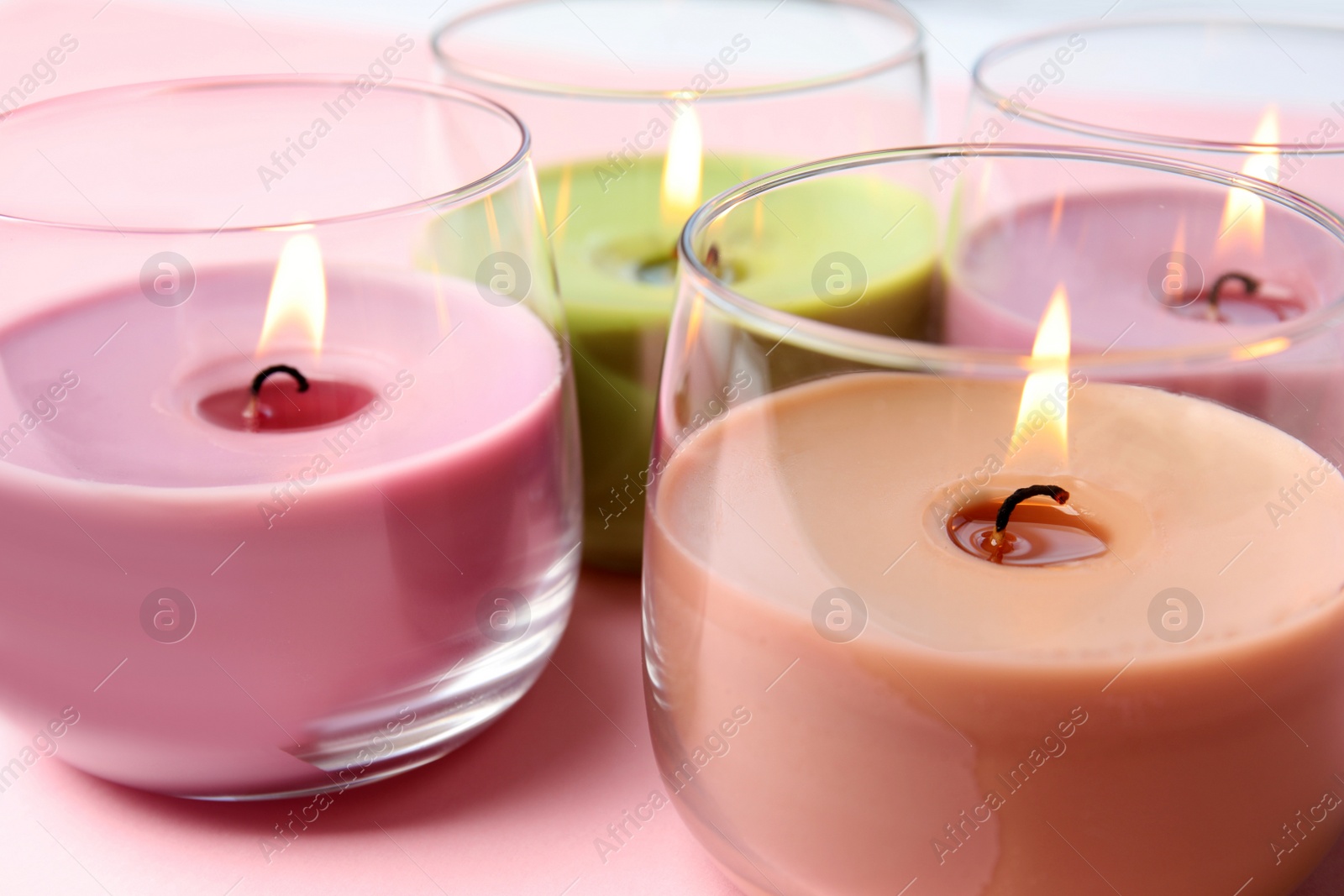 Photo of Burning wax candles in glass holders on pink background, closeup