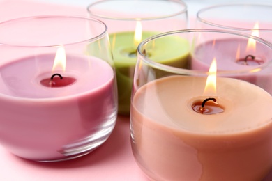 Photo of Burning wax candles in glass holders on pink background, closeup