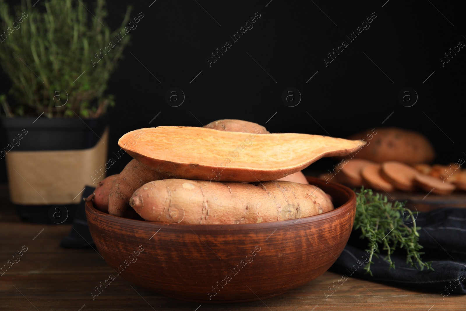 Photo of Cut and whole sweet potatoes in bowl on wooden table
