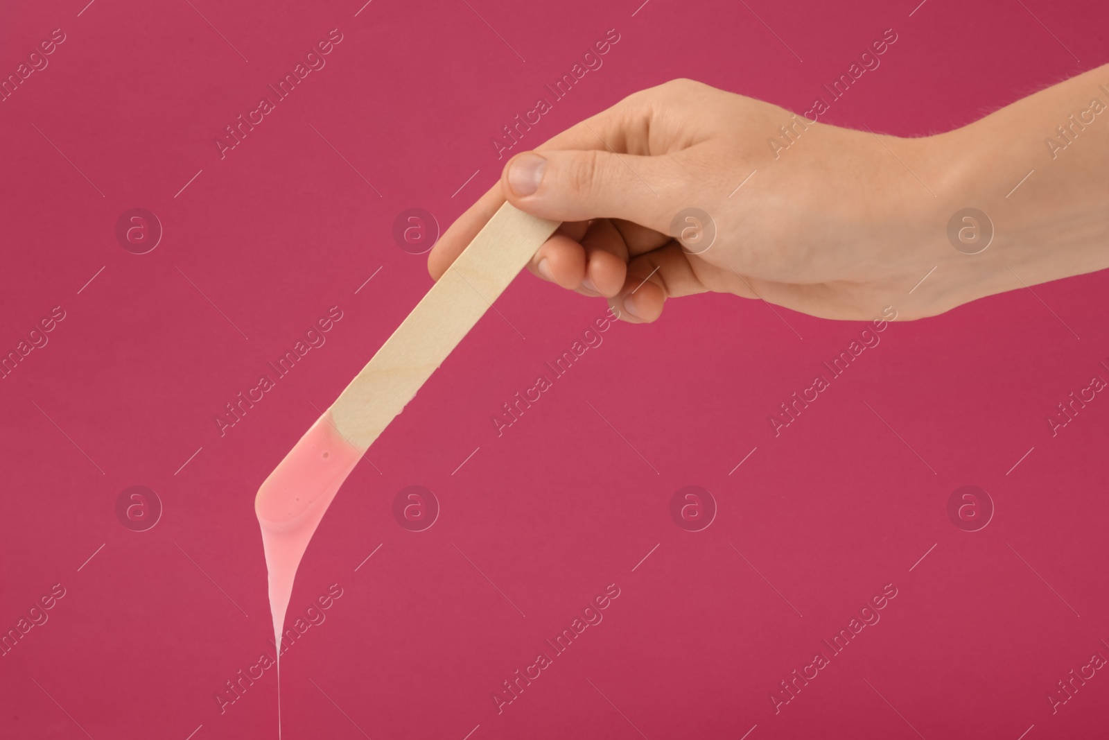 Photo of Woman holding spatula with hot depilatory wax on fuchsia background, closeup