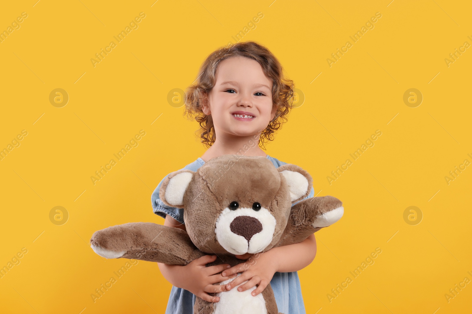 Photo of Cute little girl with teddy bear on orange background