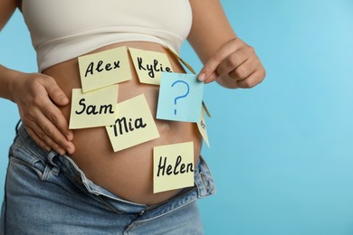 Photo of Pregnant woman with different baby names on belly against light blue background, closeup