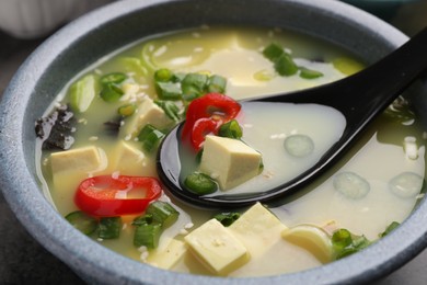 Photo of Bowl of delicious miso soup with tofu and spoon on table, closeup