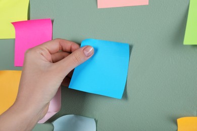 Photo of Woman sticking light blue note on grey wall, closeup