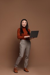 Full length portrait of smiling woman with laptop on brown background