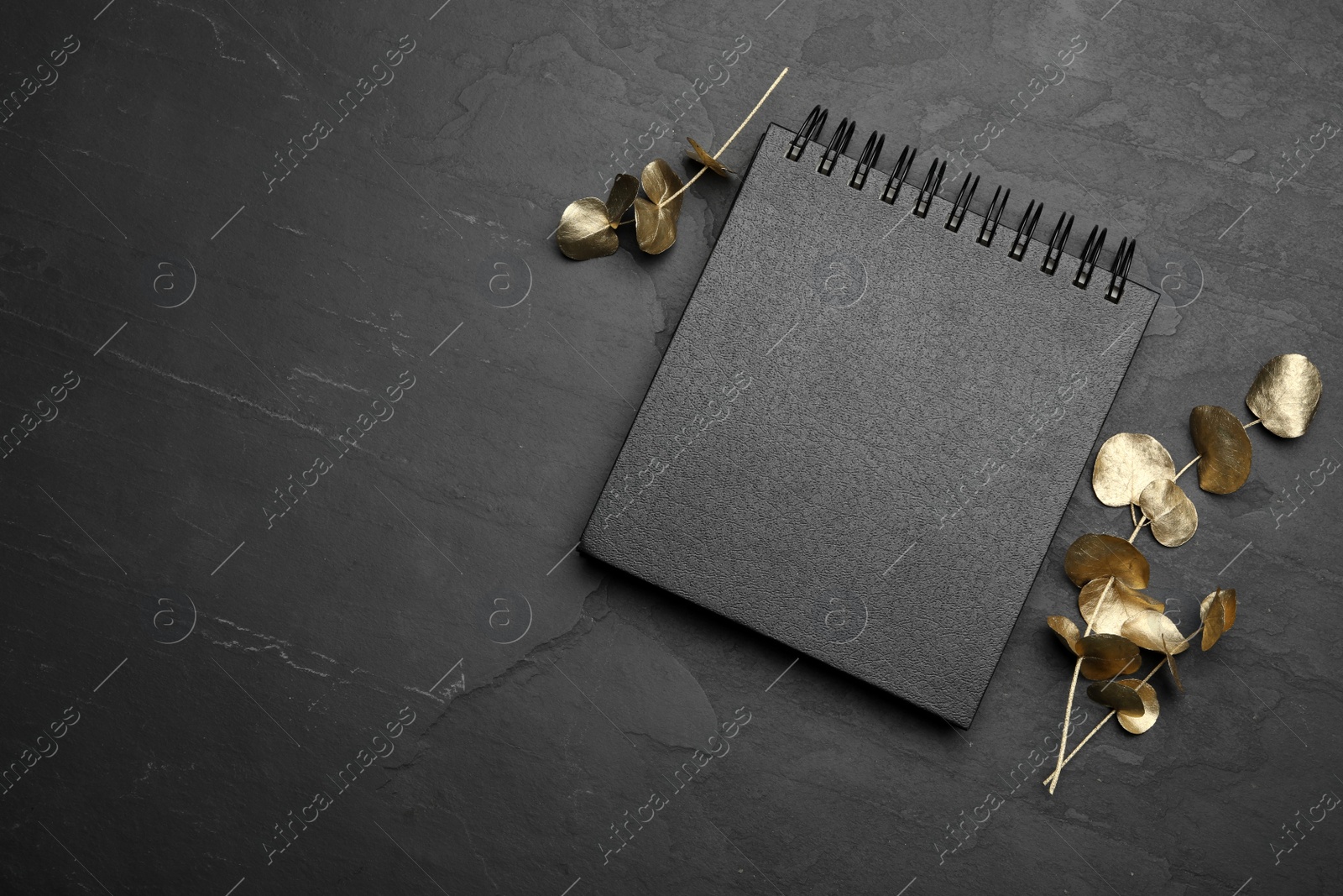 Photo of Stylish black notebook and golden branches on table, flat lay. Space for text