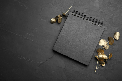 Photo of Stylish black notebook and golden branches on table, flat lay. Space for text