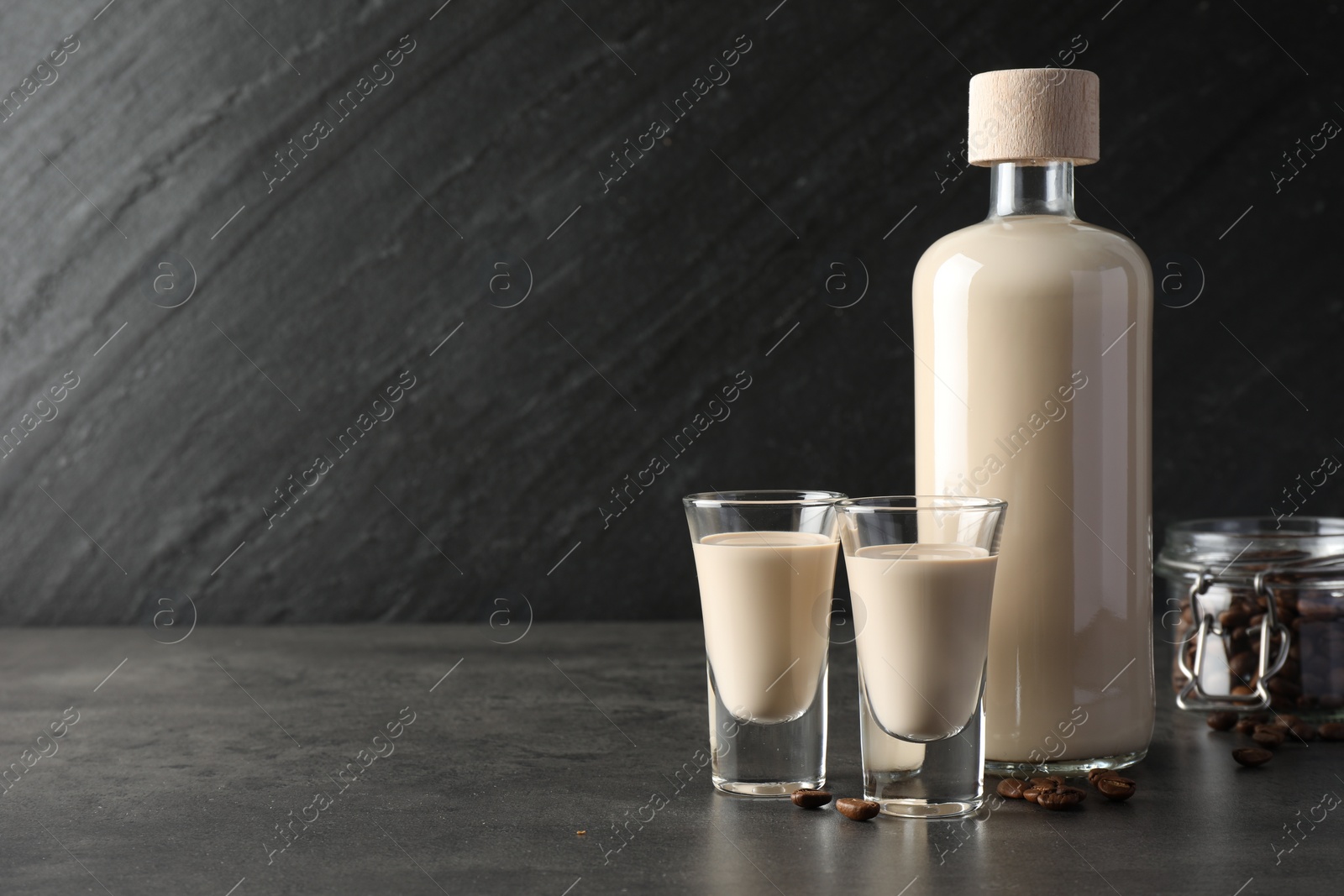 Photo of Coffee cream liqueur in glasses, bottle and beans on grey table, space for text