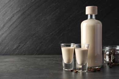 Coffee cream liqueur in glasses, bottle and beans on grey table, space for text