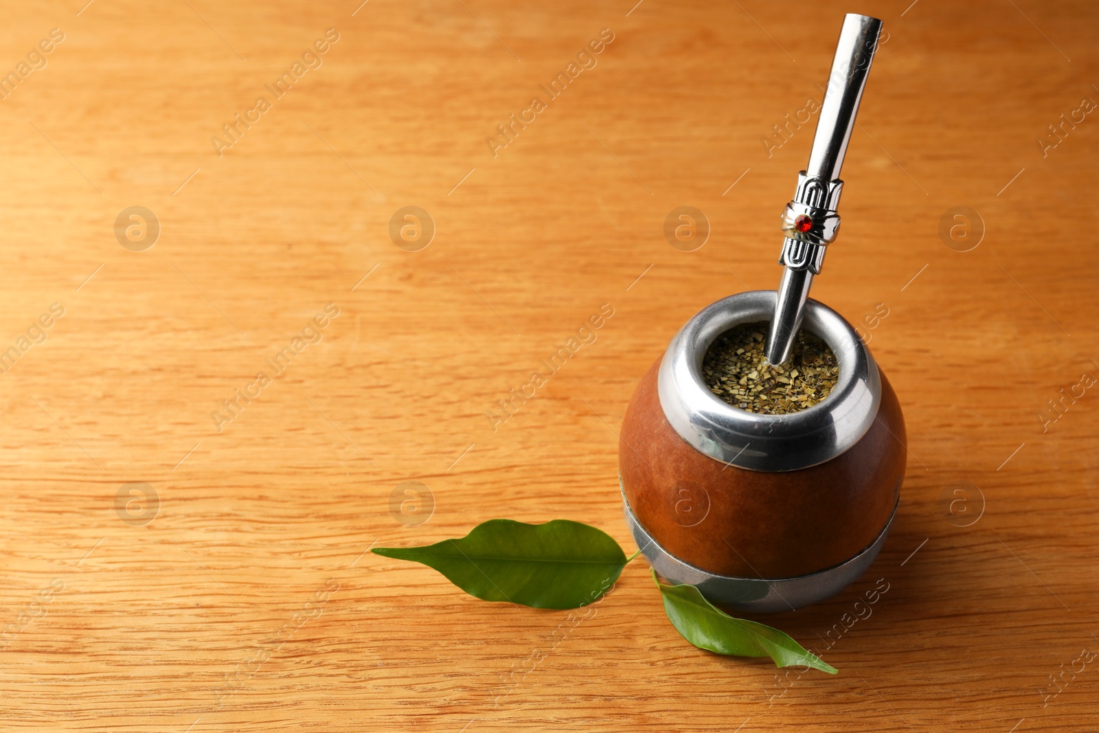 Photo of Calabash with mate tea and bombilla on wooden table. Space for text