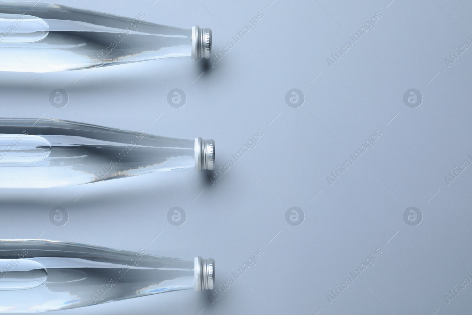 Photo of Glass bottles with water on white background, flat lay. Space for text