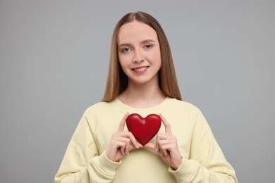 Photo of Happy young woman holding red heart on light grey background