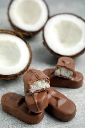 Photo of Delicious milk chocolate candy bars with coconut filling on grey table, closeup