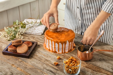 Photo of Young woman decorating delicious caramel cake at table