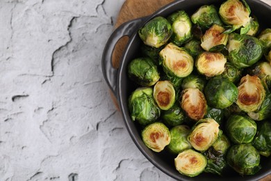 Photo of Delicious roasted Brussels sprouts in baking dish on white textured table, top view. Space for text