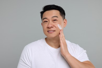 Photo of Handsome man applying cream onto his face on light grey background