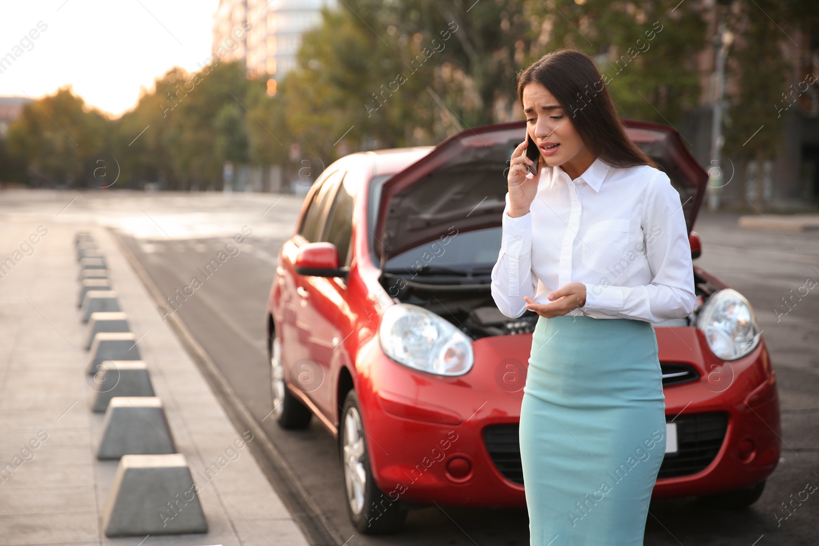 Photo of Stressed woman talking on phone near broken car outdoors