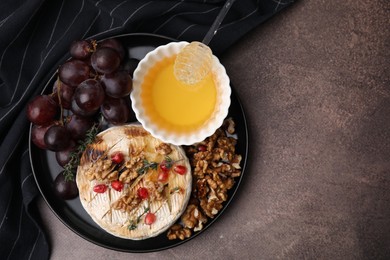 Photo of Plate with tasty baked camembert, honey, grapes, walnuts and pomegranate seeds on brown textured table, top view. Space for text