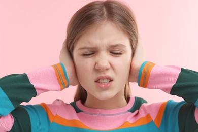 Hearing problem. Little girl suffering from ear pain on pink background