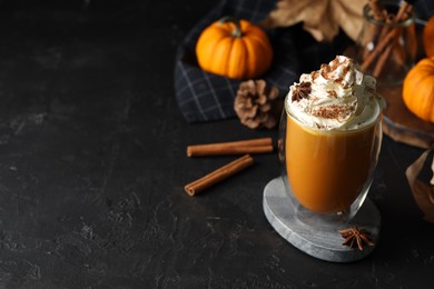 Photo of Glass of pumpkin spice latte with whipped cream and ingredients on black table. Space for text