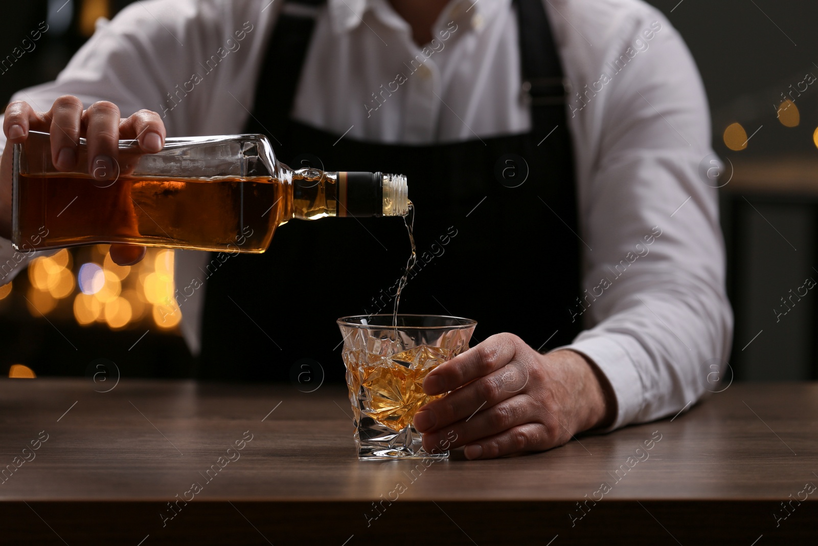 Photo of Bartender pouring whiskey from bottle into glass at bar counter indoors, closeup