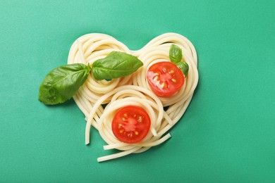 Photo of Heart made of tasty spaghetti, tomato and basil on green background, top view