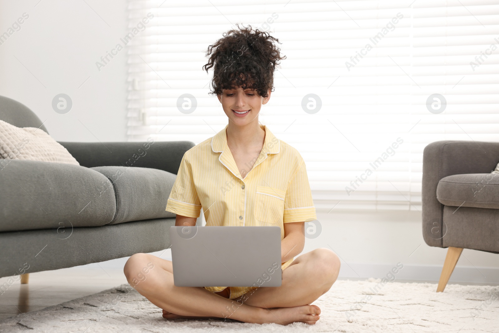 Photo of Beautiful young woman in stylish pyjama using laptop on floor at home