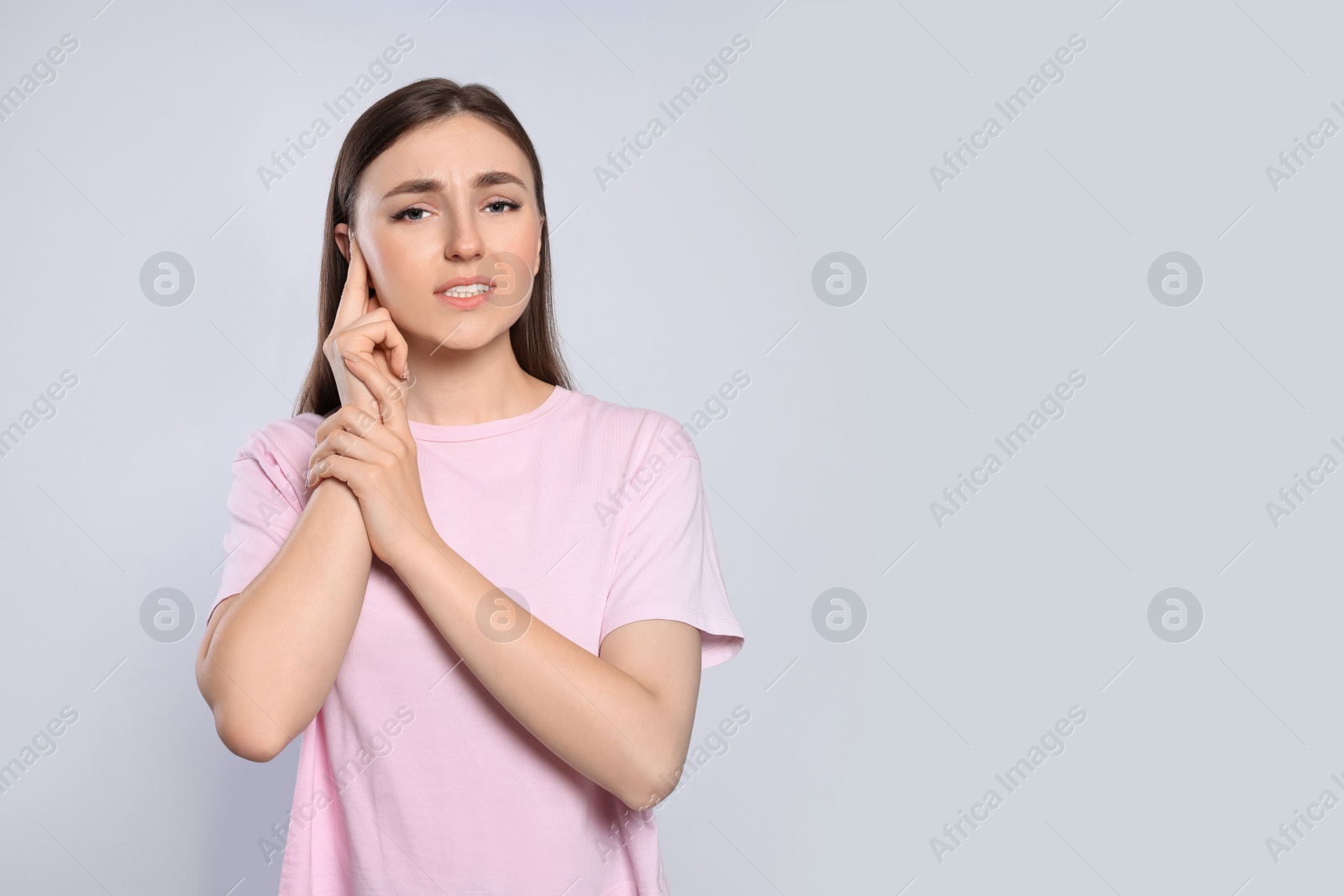 Photo of Young woman suffering from ear pain on light grey background. Space for text