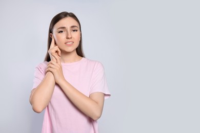 Photo of Young woman suffering from ear pain on light grey background. Space for text