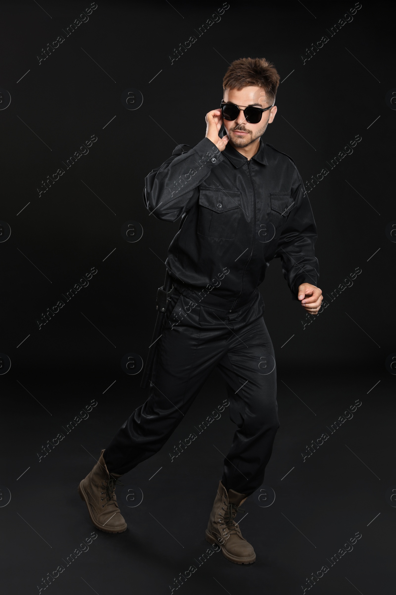 Photo of Male security guard in uniform using radio earpiece on dark background