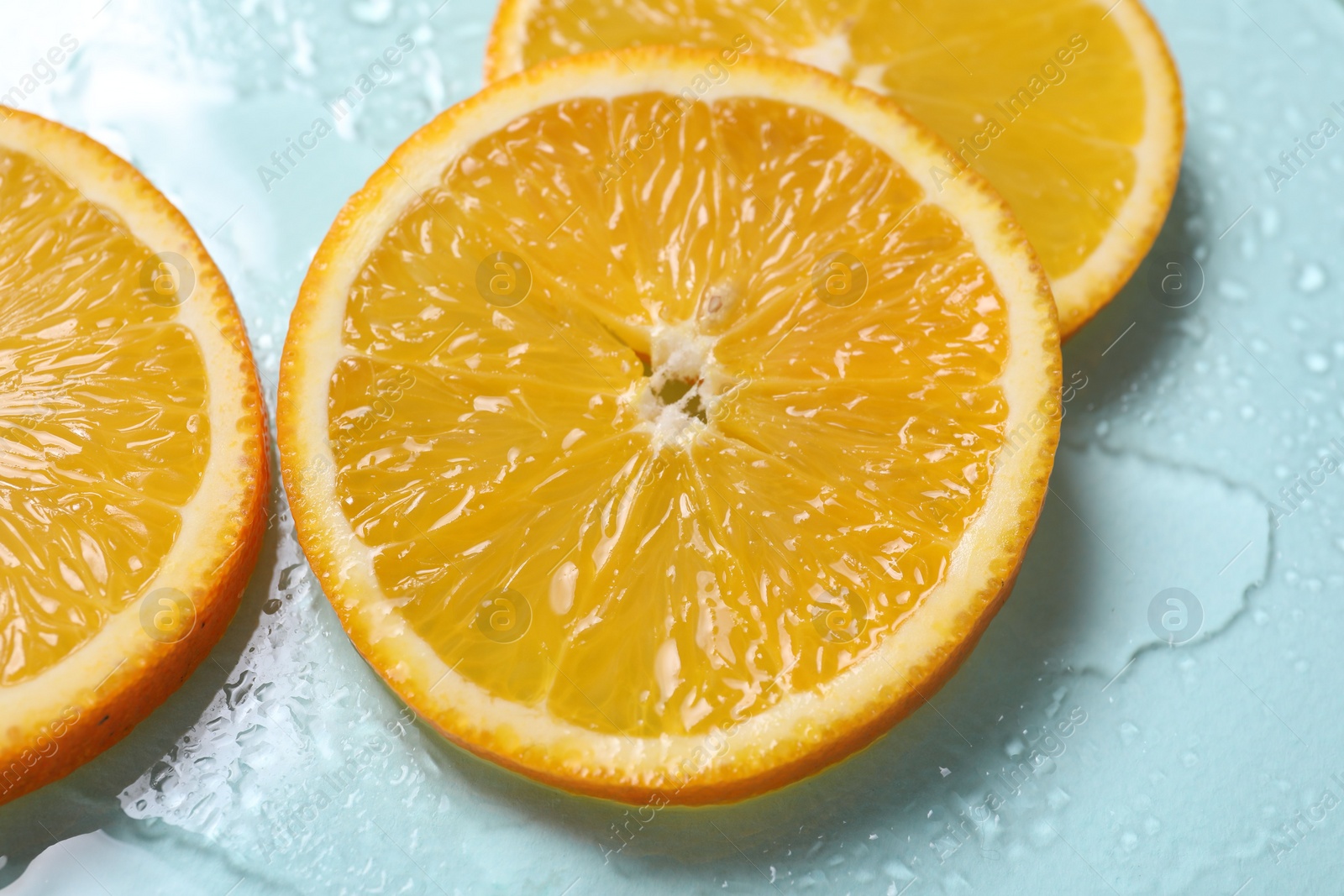 Photo of Slices of juicy orange and water on light blue background, closeup