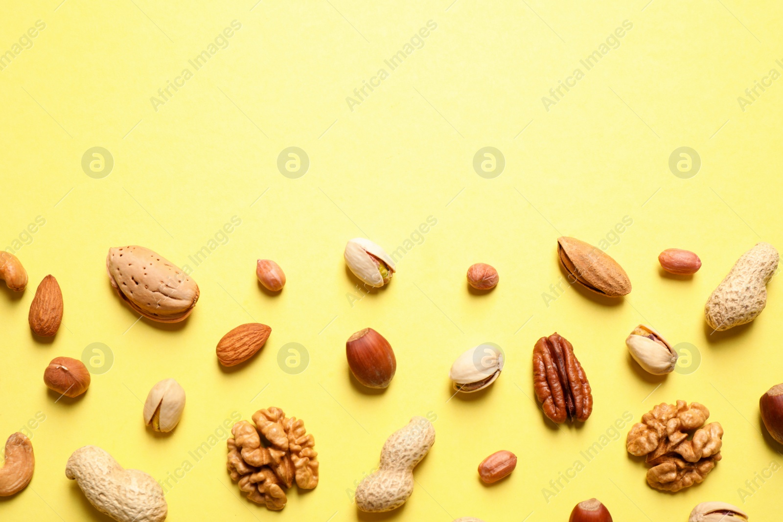 Photo of Different delicious nuts on yellow background, flat lay. Space for text