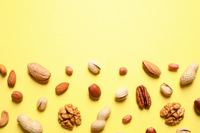 Different delicious nuts on yellow background, flat lay. Space for text