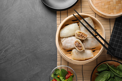 Photo of Delicious cabbage rolls in bamboo steamer on grey table, flat lay. Space for text