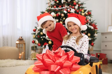 Photo of Cute little children playing with toy car in room decorated for Christmas