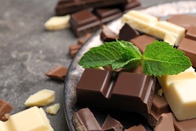 Photo of Different kinds of chocolate with mint on gray table