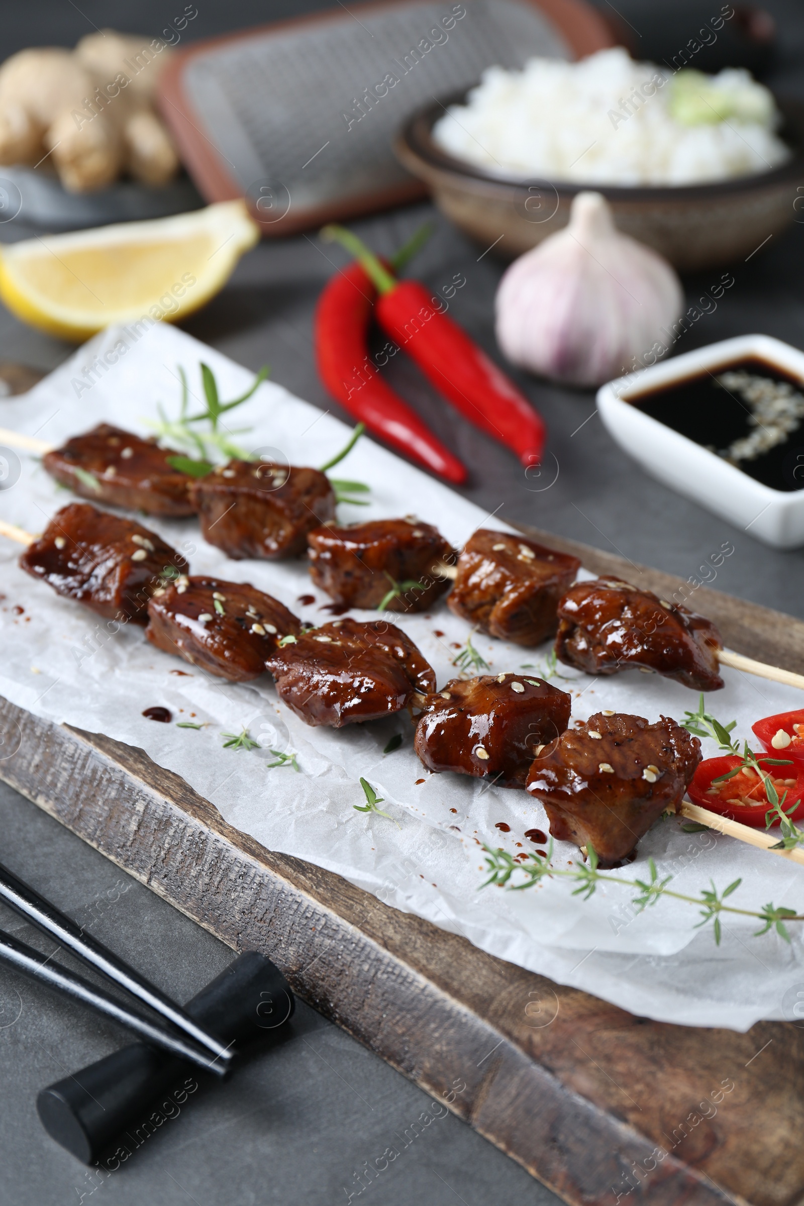Photo of Skewers with pieces of tasty chicken meat glazed in soy sauce and other products on grey table, closeup