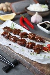 Photo of Skewers with pieces of tasty chicken meat glazed in soy sauce and other products on grey table, closeup