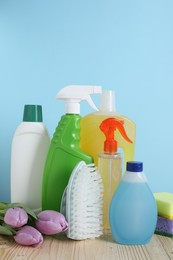 Spring cleaning. Different detergents, tools and beautiful flowers on wooden table against light blue background