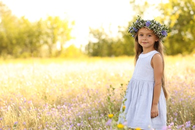 Cute little girl wearing flower wreath outdoors, space for text. Child spending time in nature