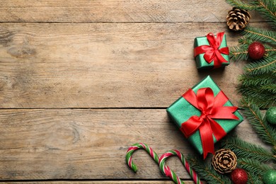 Photo of Gift boxes, candy canes, fir tree branches and Christmas decor on wooden table, flat lay. Space for text