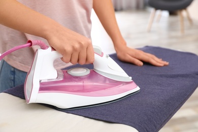 Photo of Young woman ironing clothes on board at home, closeup