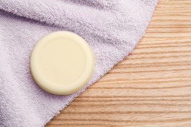 Photo of Solid shampoo bar and towel on wooden table, top view. Space for text